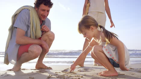 Familia-Feliz-Jugando-En-La-Playa-Dibujando-En-La-Arena-Al-Atardecer