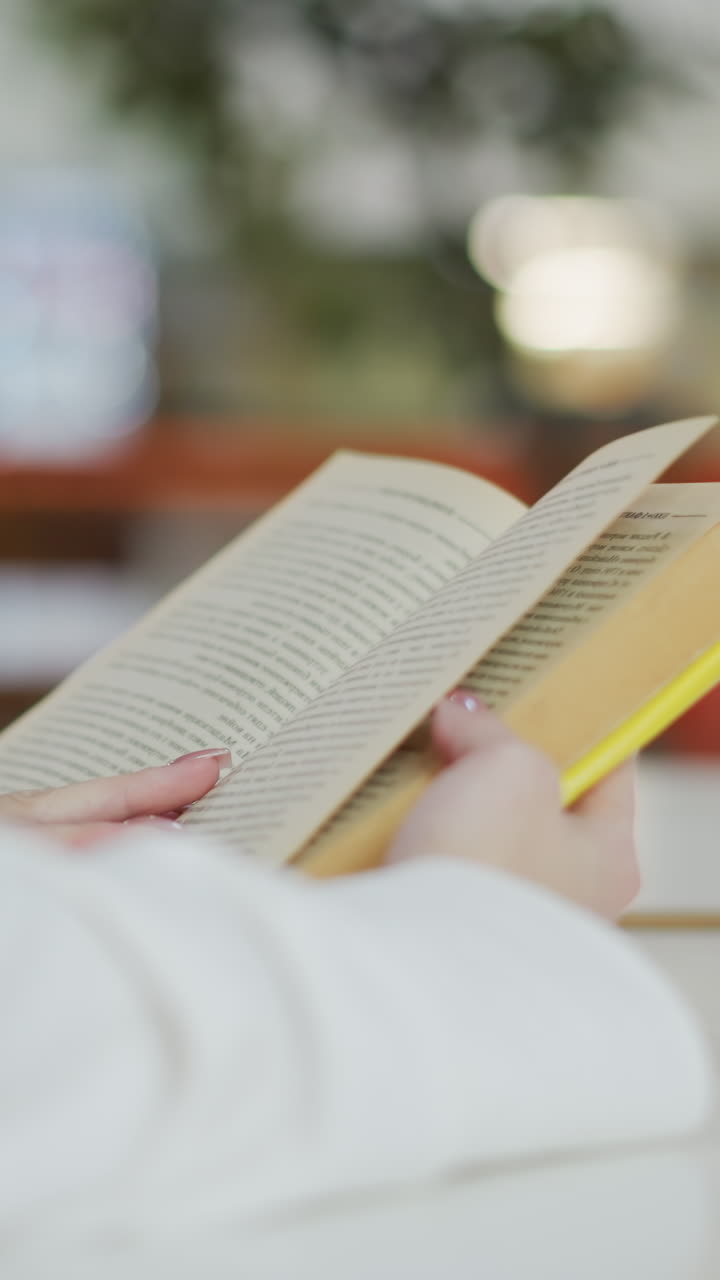 close-up de manos hojeando páginas de un libro mientras están sentados en un centro comercial ocupado con una taza de café en la mesa, con un fondo borroso con personas moviéndose