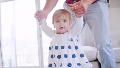 father helping daughter learn to walk at home, front view