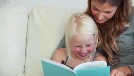 girl laughing as she reads a book with her mother