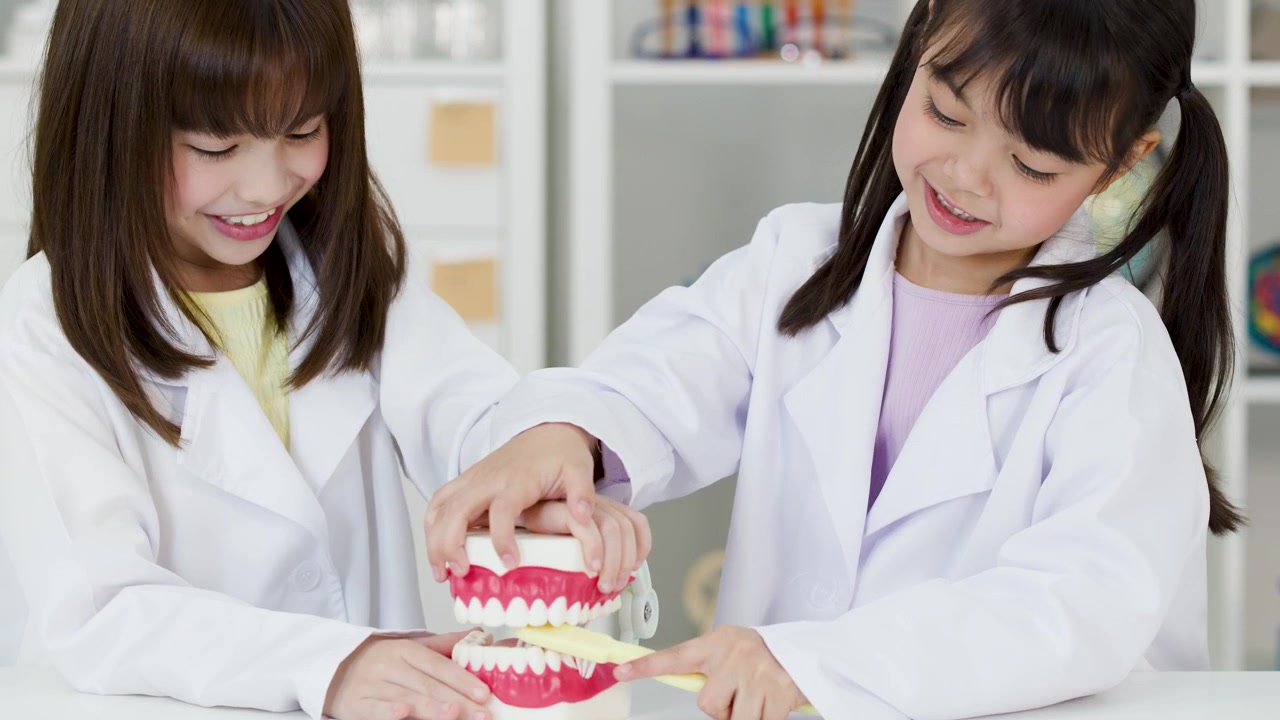 白い白衣を着た2人の若いアジア人学生が、歯科模型を使って歯磨きの練習をしています。