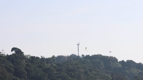 multiple paragliders flying above a lush forest