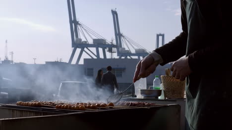 Street food vendor grilling skewers with port cranes in the background