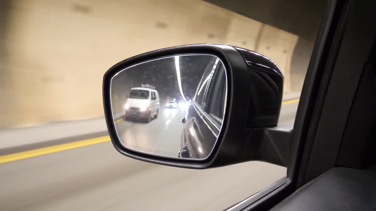 Inside a tunnel looking in the side mirror of a car