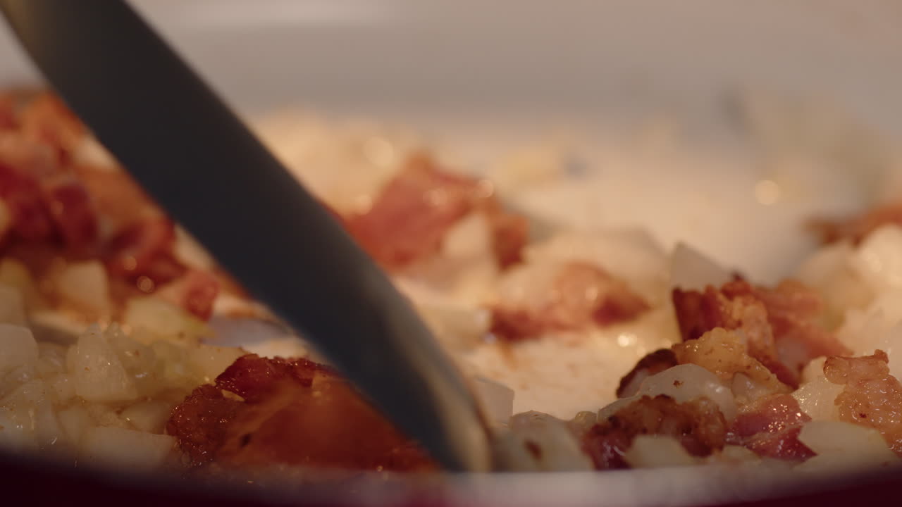 Chopped bacon and minced onion being saut&eacute;ed in a hot pan with a spoon