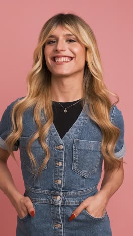 happy transgender woman in denim dress against pink background