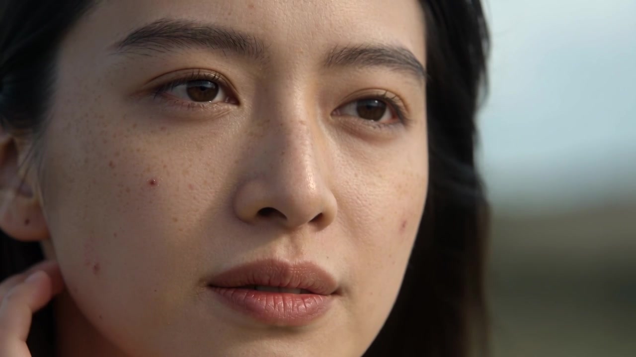 そよ風を感じながら、右手で髪をとかし、地平線に向かって目を閉じている女性。ピンクのヘアクリップが見える。