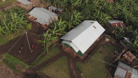 Aerial-drone-shot-of-children-running-away-and-playing-together-on-a-village-in-Uganda,-Africa