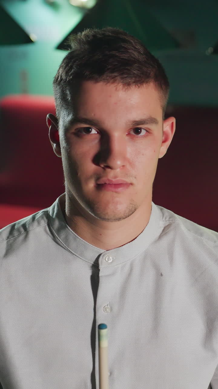 joven con camisa blanca mantiene la posición enfocada, sosteniendo el taco en la sala de billar débilmente iluminada. la atmósfera estratégica e intensa agrega profundidad al momento mientras el jugador se prepara para el siguiente movimiento