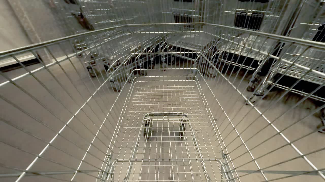 POV shot: a customer driving an empty cart inside the aisle of a shopping mart, putting it back in the row of used ones