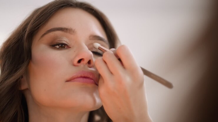 Focused woman applies shadow on eyelid looking in mirror