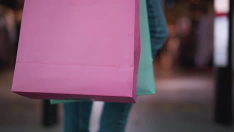 close-up of pink shopping bag with mint bag slightly visible, carried by shopper walking through vibrant shopping mall, background features bustling activity