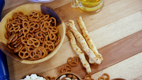 bowl of snacks, football and glass of beer on wooden table 4k