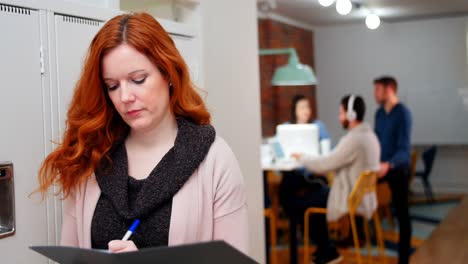 Female-executive-writing-in-file-in-locker-room