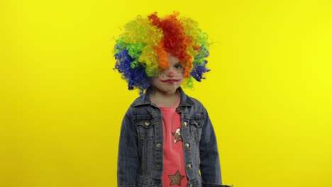 niña pequeña payaso en peluca arco iris enojado de pie y esperando algo. halloween