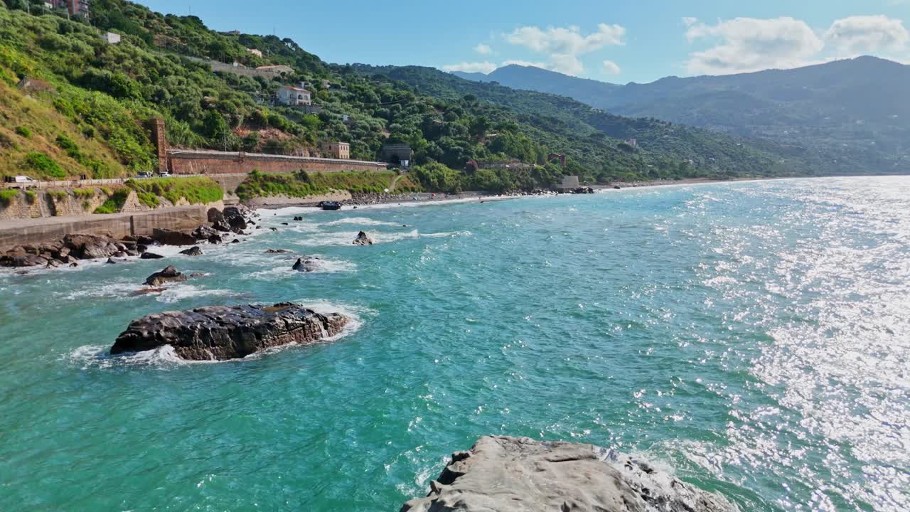 Scenic coastline under blue sky with distant mountains and waves crashing