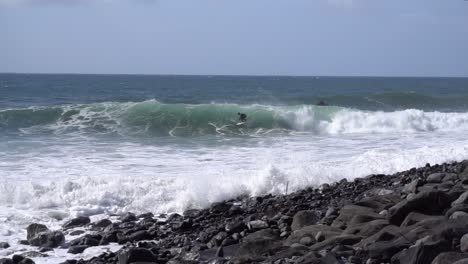 slow motion footage of a surfer getting a big wave at a rocky beach