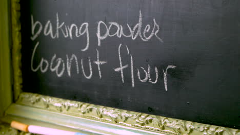 a chalk board in a kitchen having coconut flour and baking powder written on it, serving as a reminder and a shopping list