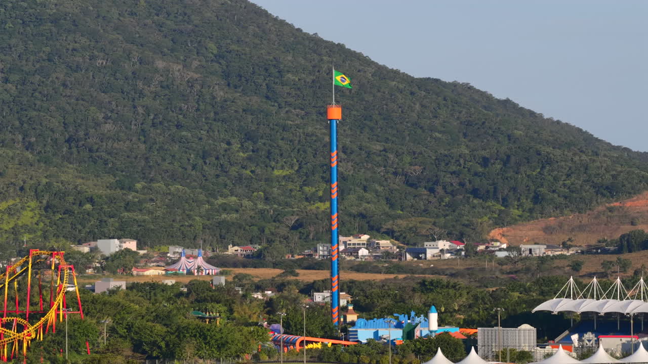 Wide drone shot frames Beto Carrero’s drop tower against towering hillside, showcasing its scale within the park’s vibrant attractions. Ideal for destination marketing