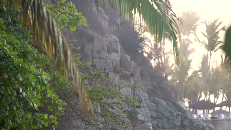 cerca del follaje tropical de la playa y el paisaje con una escarpada pared de roca de acantilado y varias palmeras en la costa arenosa