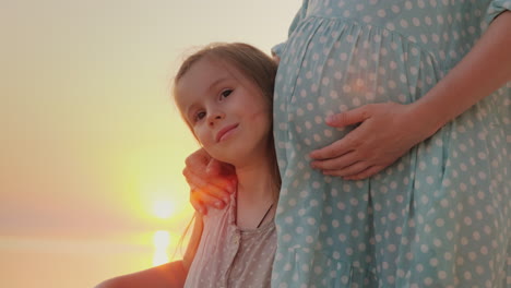 portrait of a happy caucasian girl of six years near the belly of her pregnant mother waiting for th