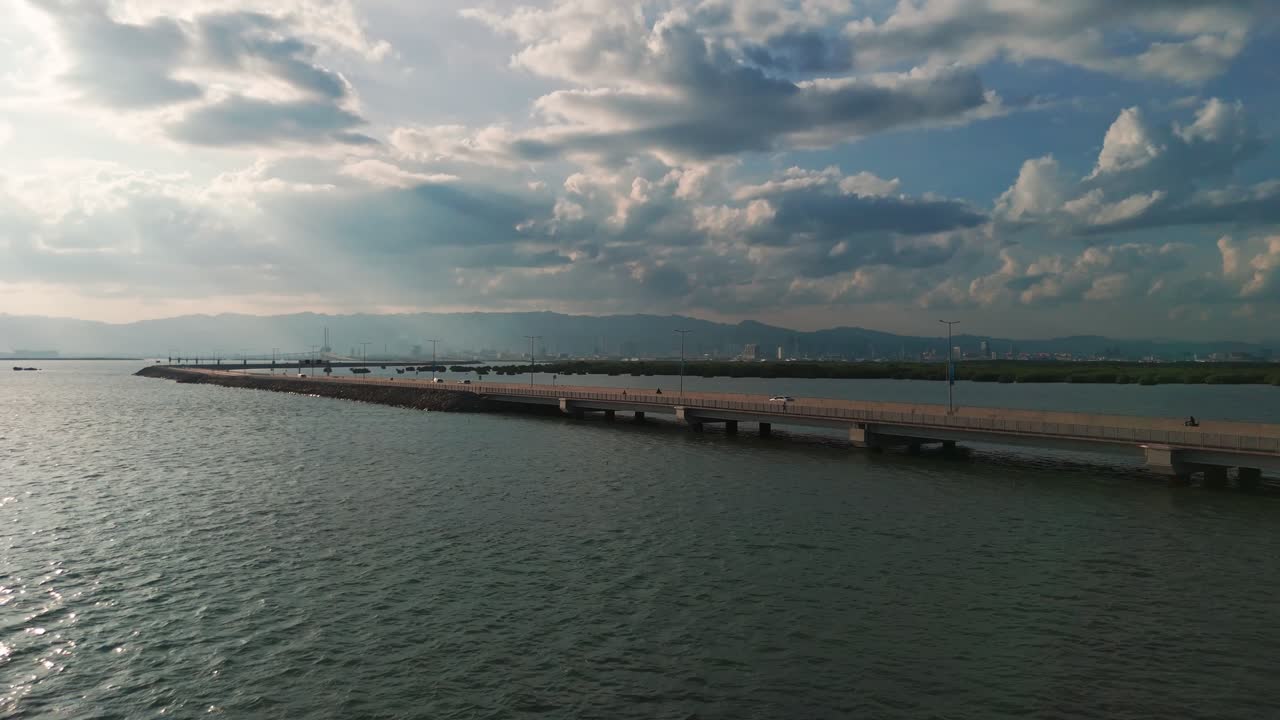 Scenic aerial view of a bridge crossing water with cars, city skyline in the background, and dramatic sky with sun rays, perfect for travel and urban projects