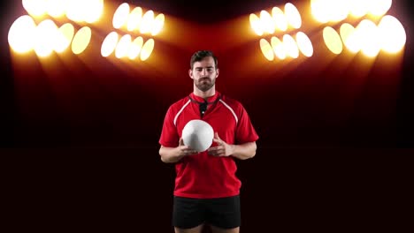 professional rugby player holding a ball in front of stadium spotlights