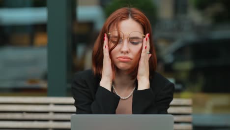 woman experiencing stress while working on a laptop in a coffee shop