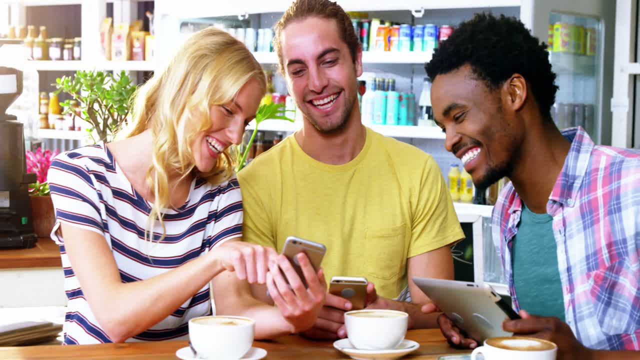 tres amigos usando teléfonos móviles mientras tienen una taza de café