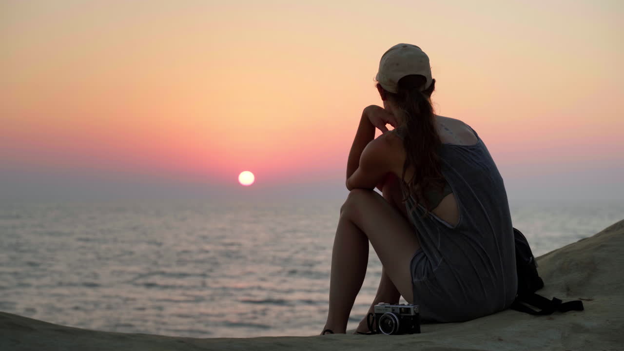 Donna con un bellissimo vestito che osserva l'alba rossa e romantica su una spiaggia sabbiosa.