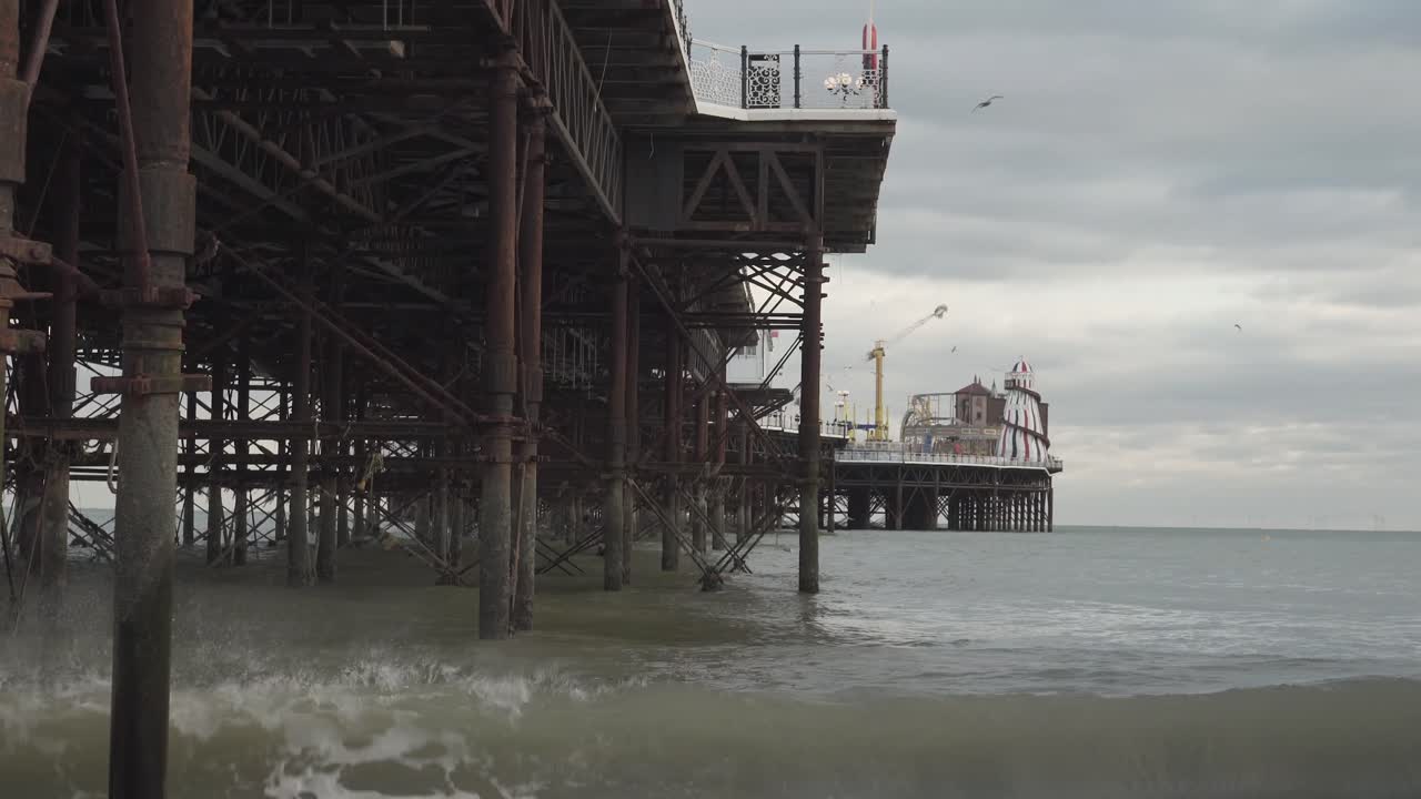 famous pier in brighton city, england uk. metal pillars, seagulls flying and cloudy sky.
