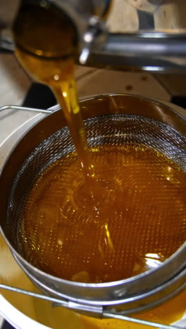 fresh honey leaking from the faucet of honey extracting machine after pumping. liquid organic product flowing on the sieve. top view. vertical video