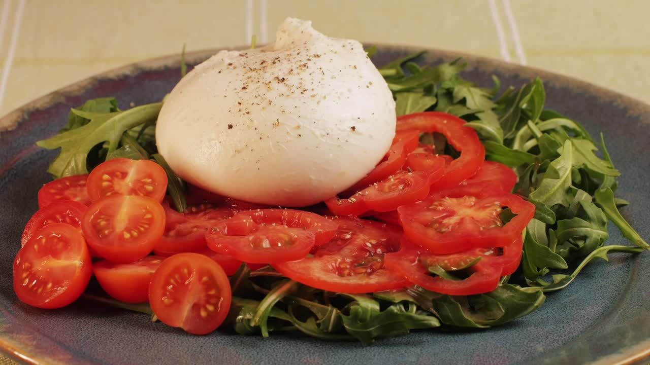Burrata or Mozzarella cheese on fresh tomatoes and green arugula on plate close-up. From Italian cow's milk cheese made from mozzarella and cream.The outer casing is solid cheese, while the inside contains stracciatella and clotted cream, giving it an unusual, soft texture.