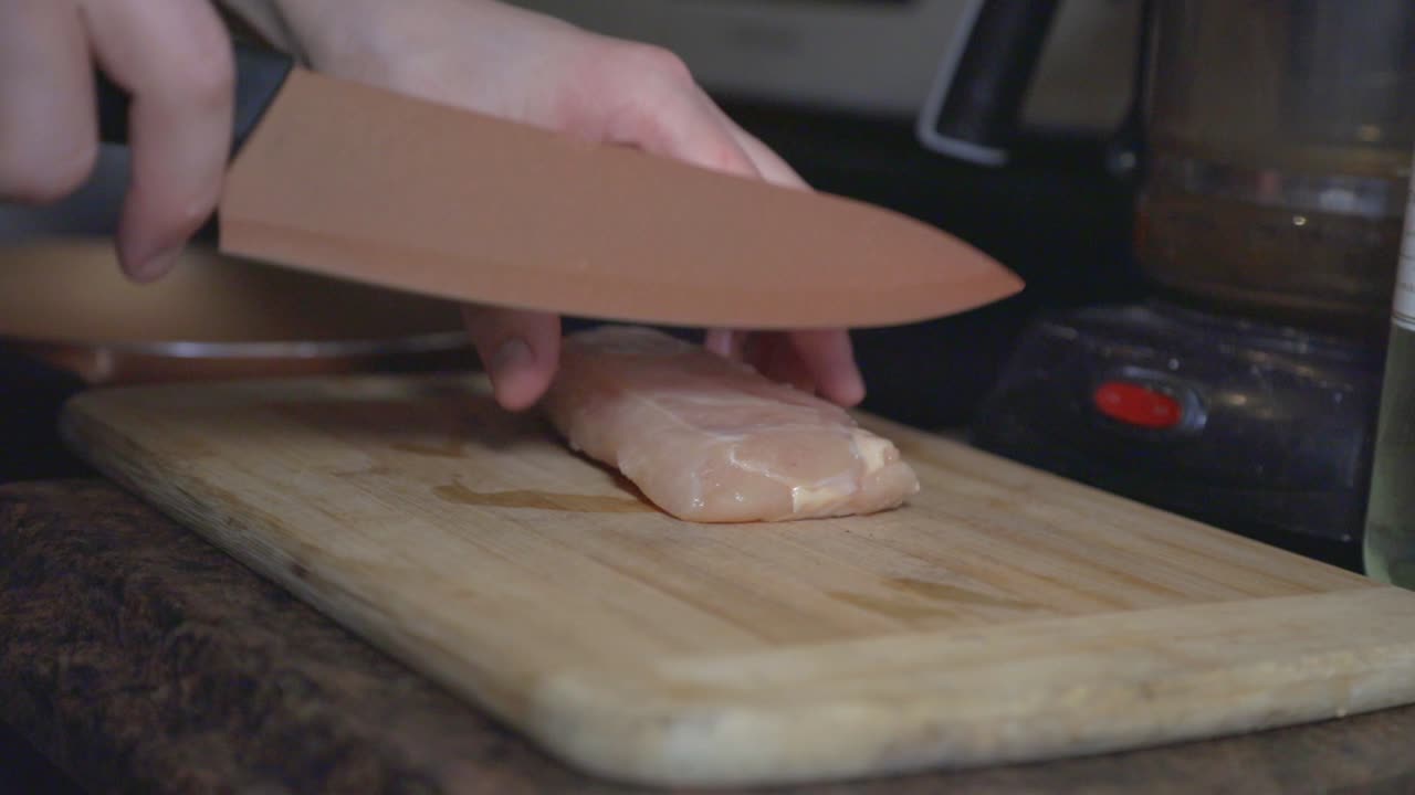 A Person Cutting Chicken Meat Into Pieces On The Wooden Board - Close Up Shot