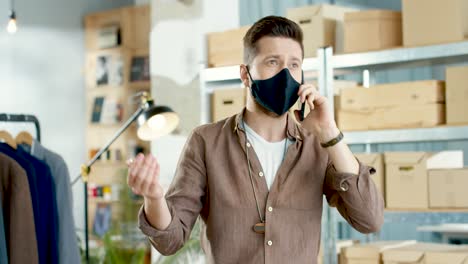 Cucasian-designer-man-in-eyeglasses-talking-on-the-phone-and-leaning-on-the-table-in-a-fashion-clothing-store