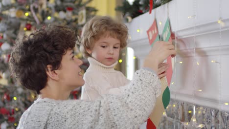 madre e hijo pequeño colgando medias navideñas de papel en una chimenea