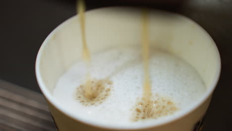 coffee pouring into a cup from a coffee machine. the video captures the detailed view of the coffee stream blending with the frothy milk in the cup