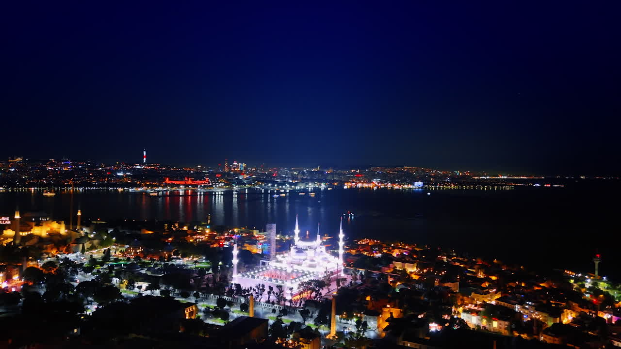 Stunning illumination of mosques in the night scenery of Istanbul, Turkey. Boat with lights moves by the waterscape. Aerial view