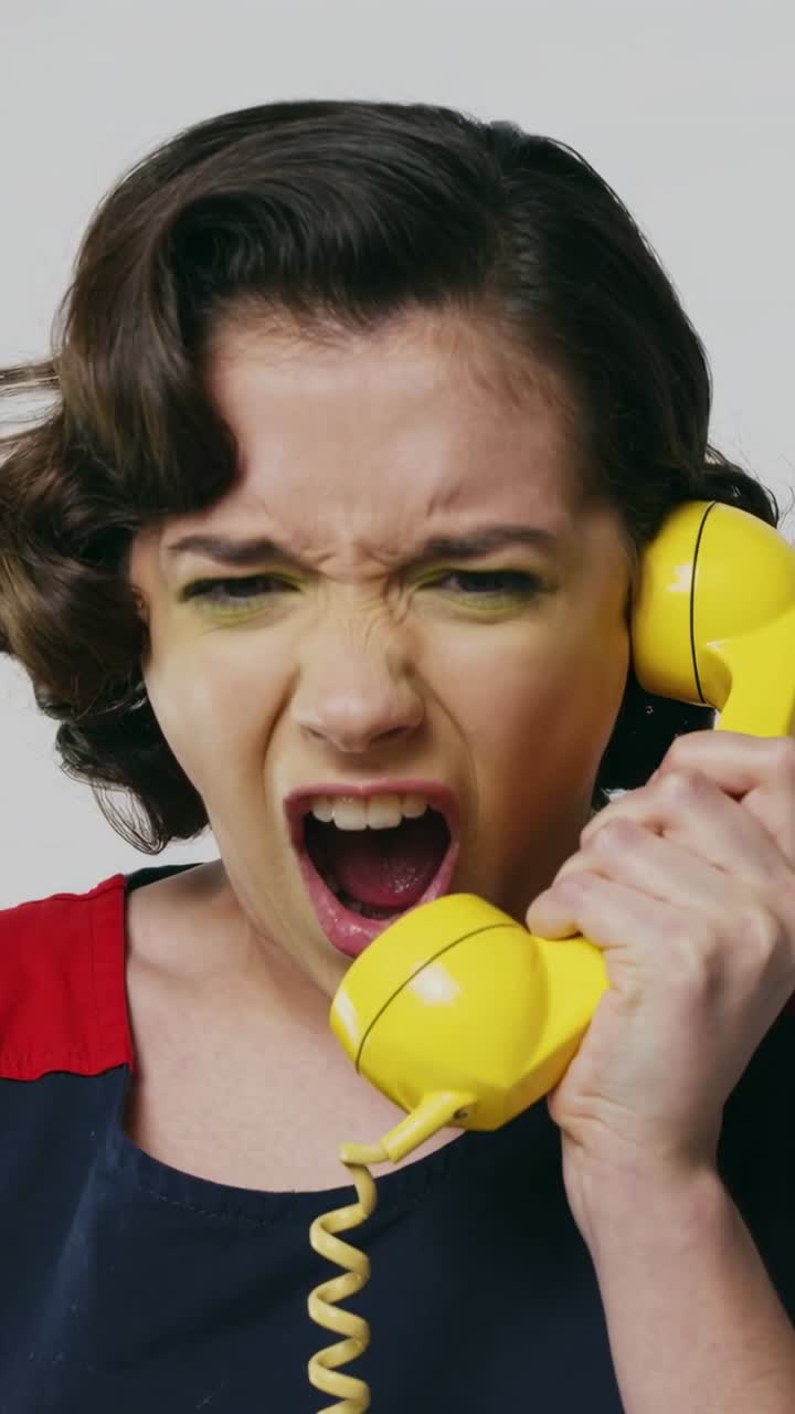Vertical video: Hearing ring, woman holding yellow handset, yelling, stunned in studio navy dress