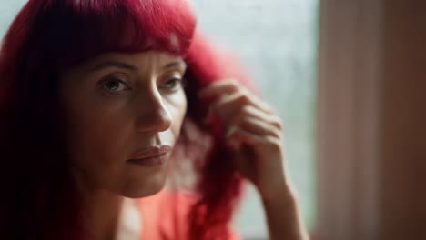 woman with red hair looking thoughtful by a window