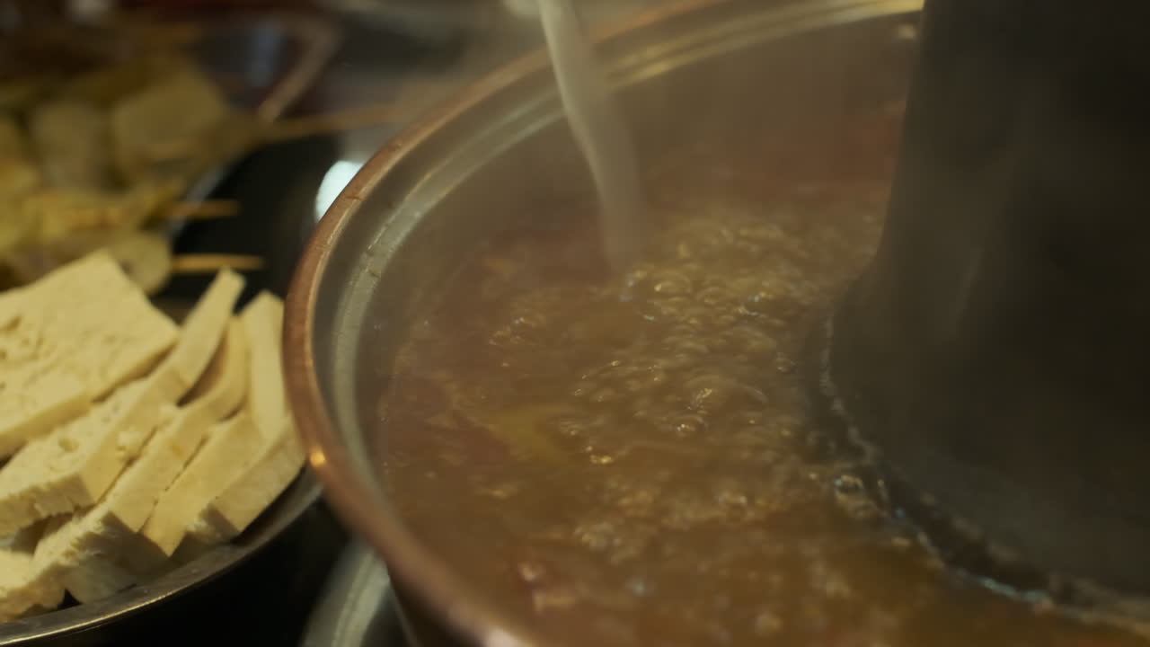 Aggiunta di brodo a un hot pot in stile cinese. Primo piano.
