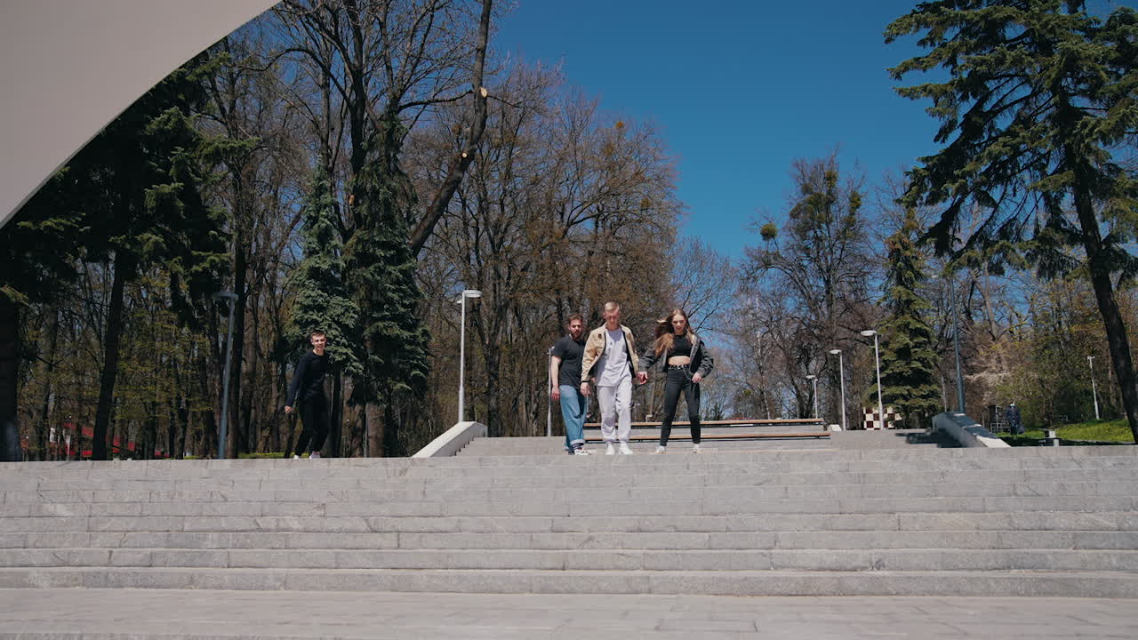 Active young people in the park. Attractive girl and guys running down on steps in the park. Happy friends spending joyful time outdoors.