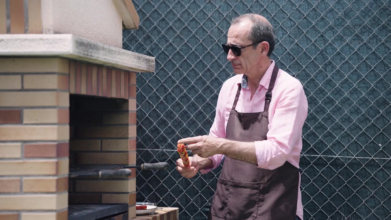 Reifer Mann grillt Fleischspieße auf einem gemauerten Außengrill