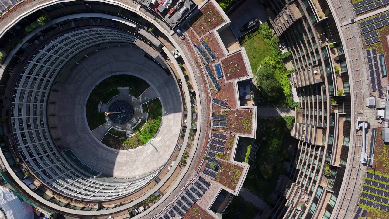 Anelli concentrici di balconi, pannelli solari e terrazze piantumate circondano il cortile centrale di un edificio residenziale modernista circolare.