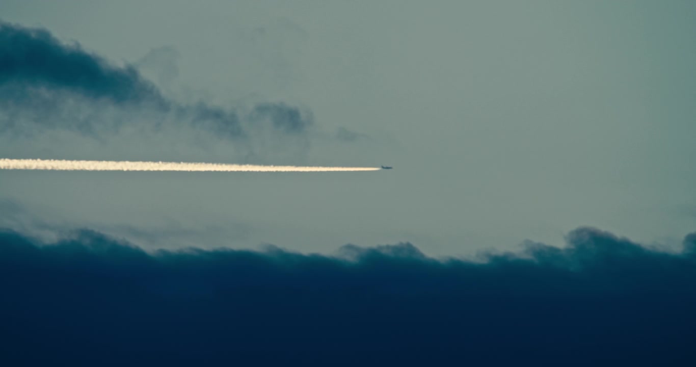 Scia di condensazione di un aereo che si estende attraverso uno strato di nuvole drammatico al crepuscolo. Cielo serale minimale con una scia di vapore ad alta quota e nuvole atmosferiche suggestive