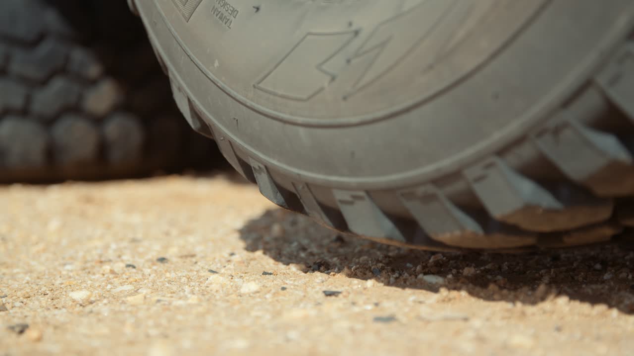 Static low close-up hand held shot of a flat punctured tire suspended above the ground after being jacked up