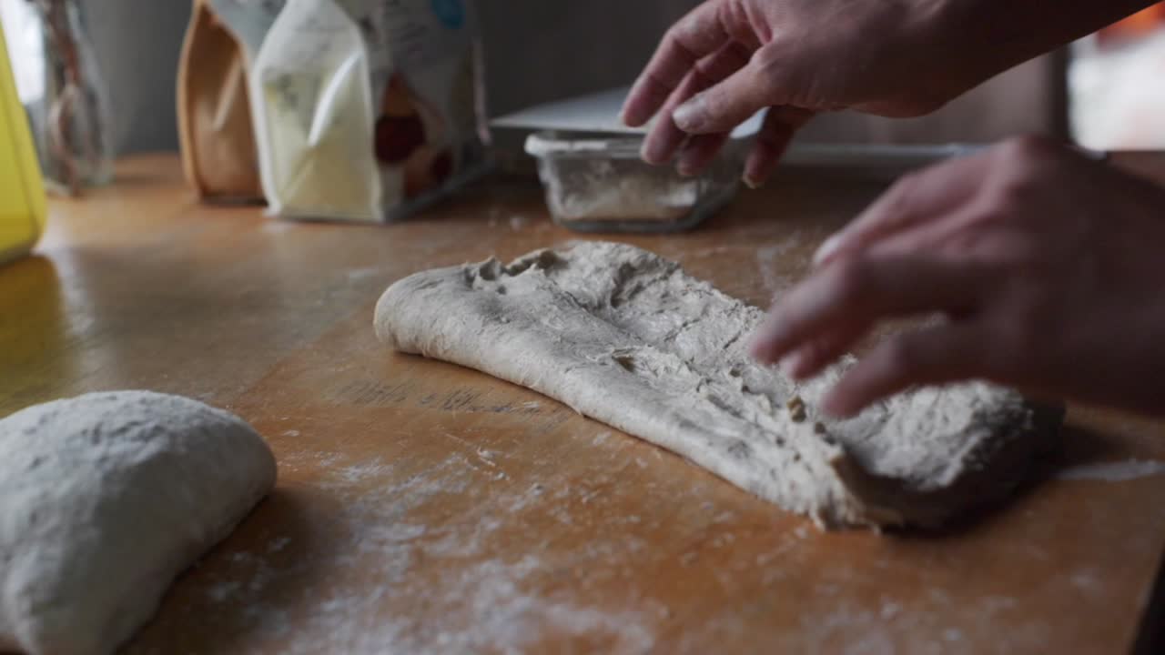 Freshly stretched dough folded in preparation for kneading on wooden kitchen table top, filmed as closeup slow motion shot