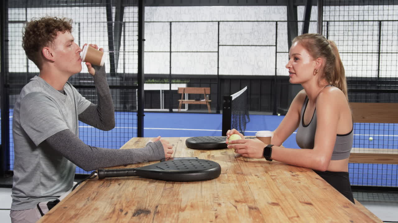 Two man and woman discussing padel tennis strategy at indoor court with rackets
