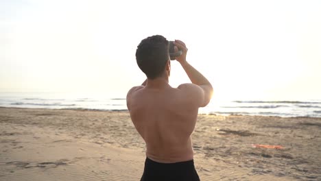 shirtless man training with kettlebell on the beach at sunrise in slow motion