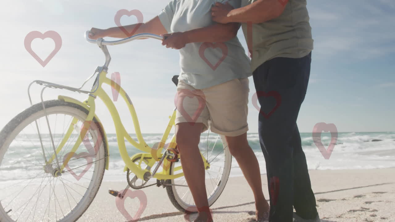 Walking on beach, elderly couple with bicycle, heart animation in scene